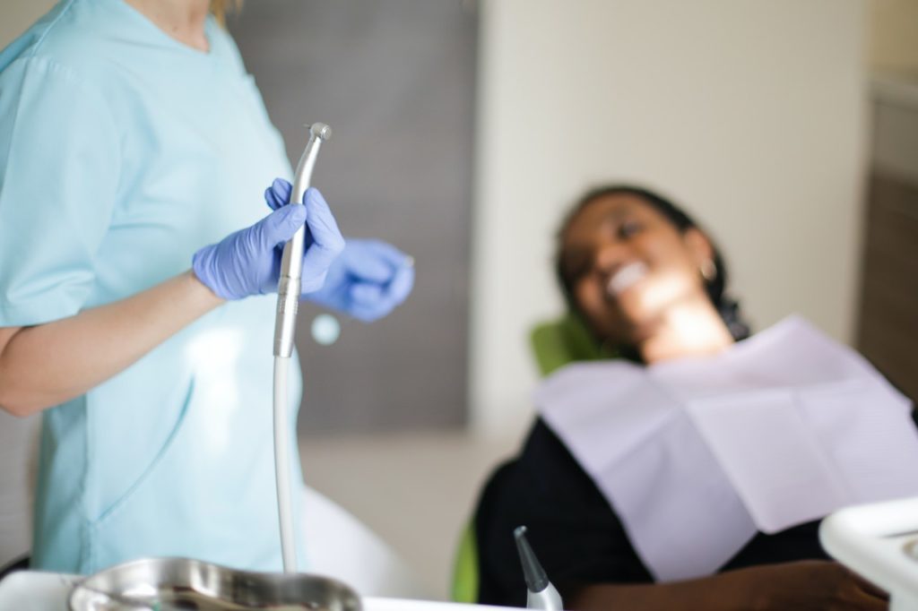 A dentist holding a tool with a patient in the background.