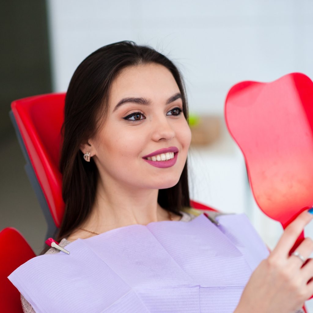 Smiling woman checking her teeth in a hand mirror