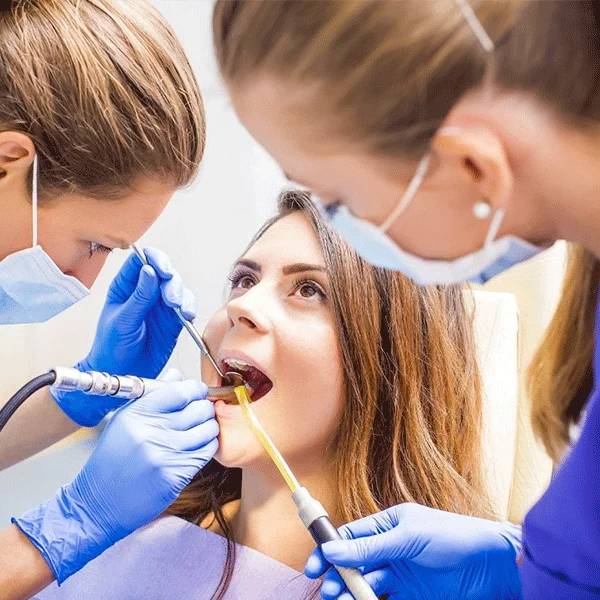 Dental professionals in gloves and masks examine a patient's teeth with dental instruments in a clinical setting
