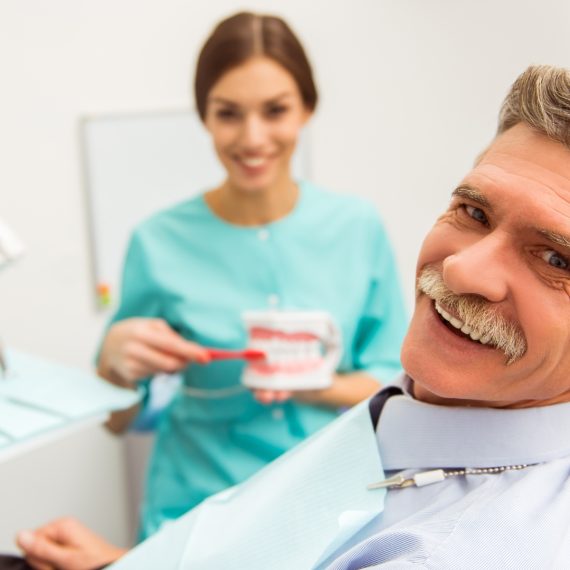 Smiling senior man and dental assistant with a denture model